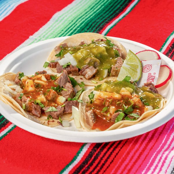Three Mi Taquito Grill tacos with meat, onions, cilantro, and salsa on a white plate.