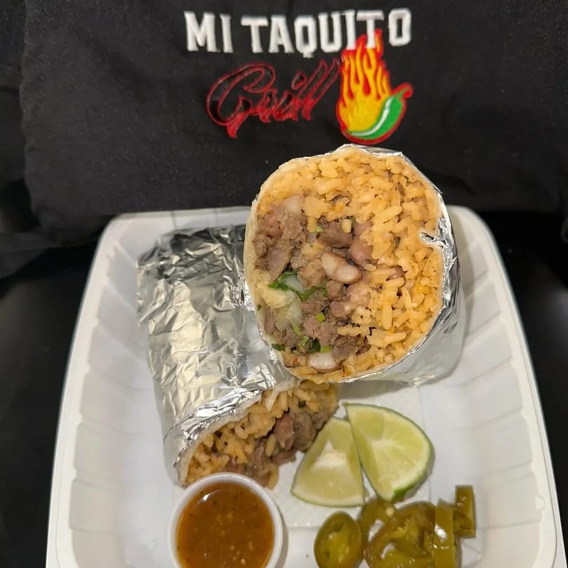 Two Mi Taquito Grill burritos, one cut open, with lime wedges, salsa, and jalapeños.