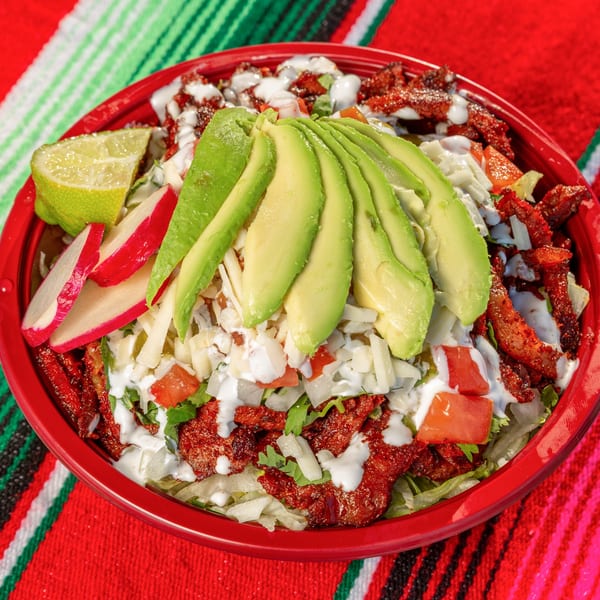 A vibrant Mi Taquito Grill Mexican salad bowl with meat, avocado, radishes, and lime.