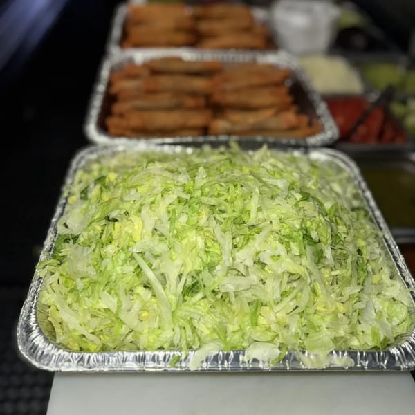 Shredded lettuce in a foil pan, with blurred pans of Mi Taquito Grill's Mexican food in the background.