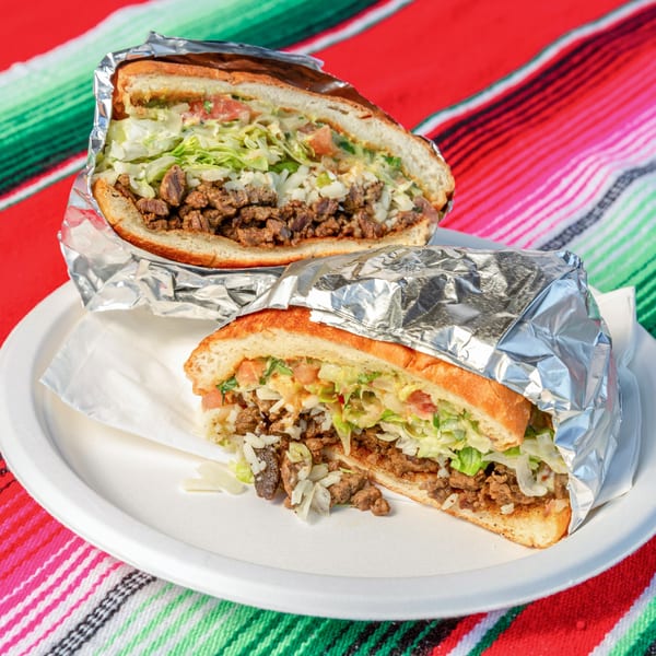 Two halves of a Mi Taquito Grill Mexican torta, filled with meat, lettuce, and cheese.
