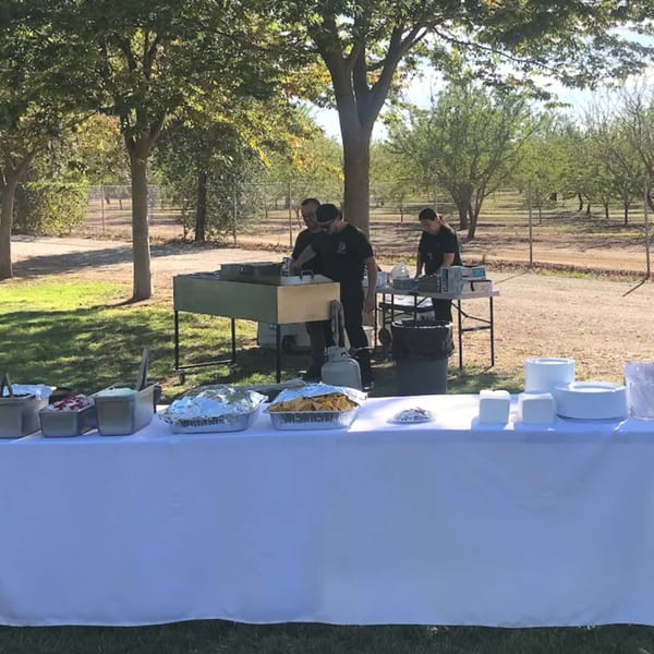 Mi Taquito Grill staff preparing Mexican food outdoors at a catering event with a buffet table.