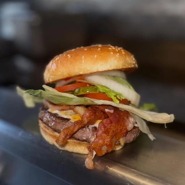 A juicy Mi Taquito Grill bacon cheeseburger with lettuce, tomato, onion, and pickles on a sesame bun.