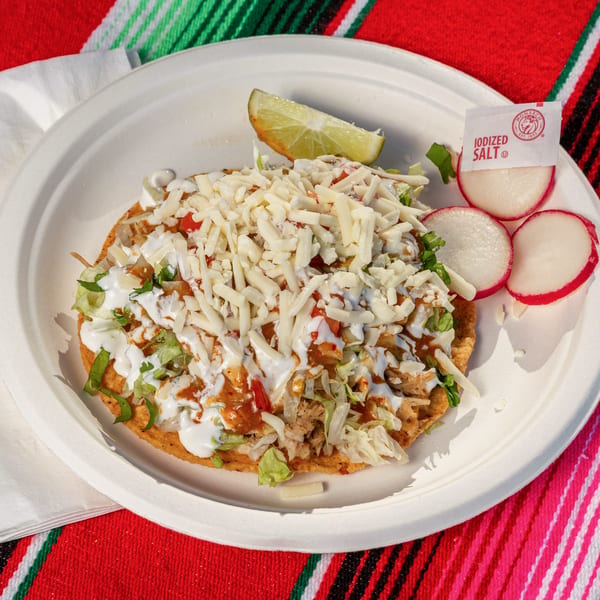 A Mi Taquito Grill tostada with shredded chicken, lettuce, cheese, sour cream, and salsa.
