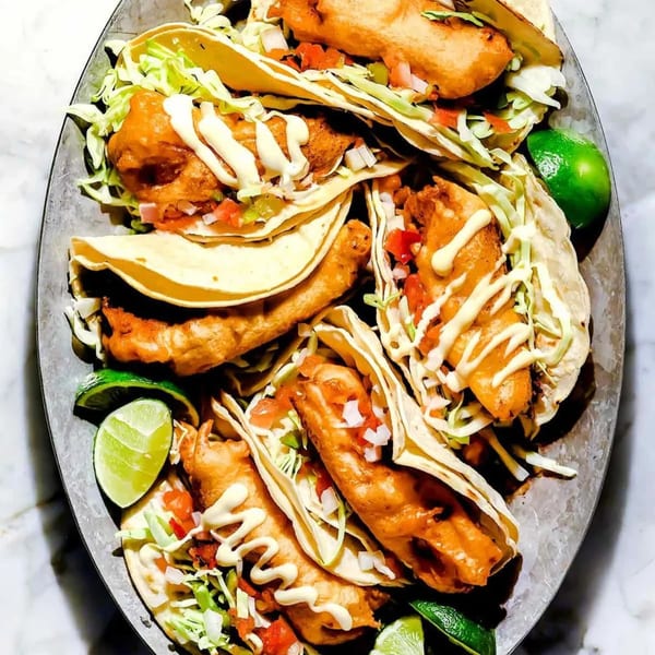 A platter of Mi Taquito Grill's fish tacos with shredded cabbage, pico de gallo, and lime wedges.